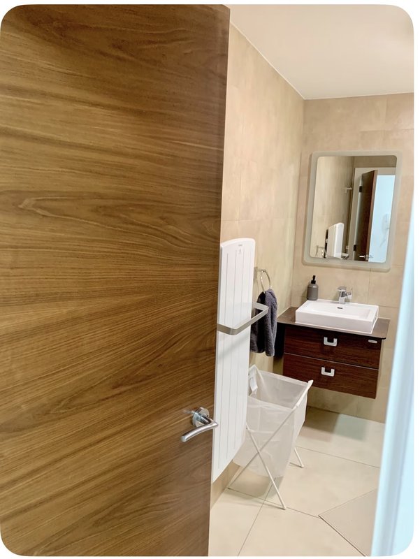 Modern bathroom with wooden door, white sink vanity, mirror and towel rack