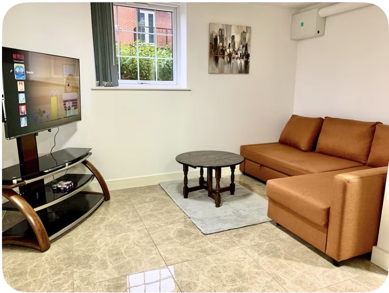 Living room with tan leather sofa, TV on stand, round coffee table and window