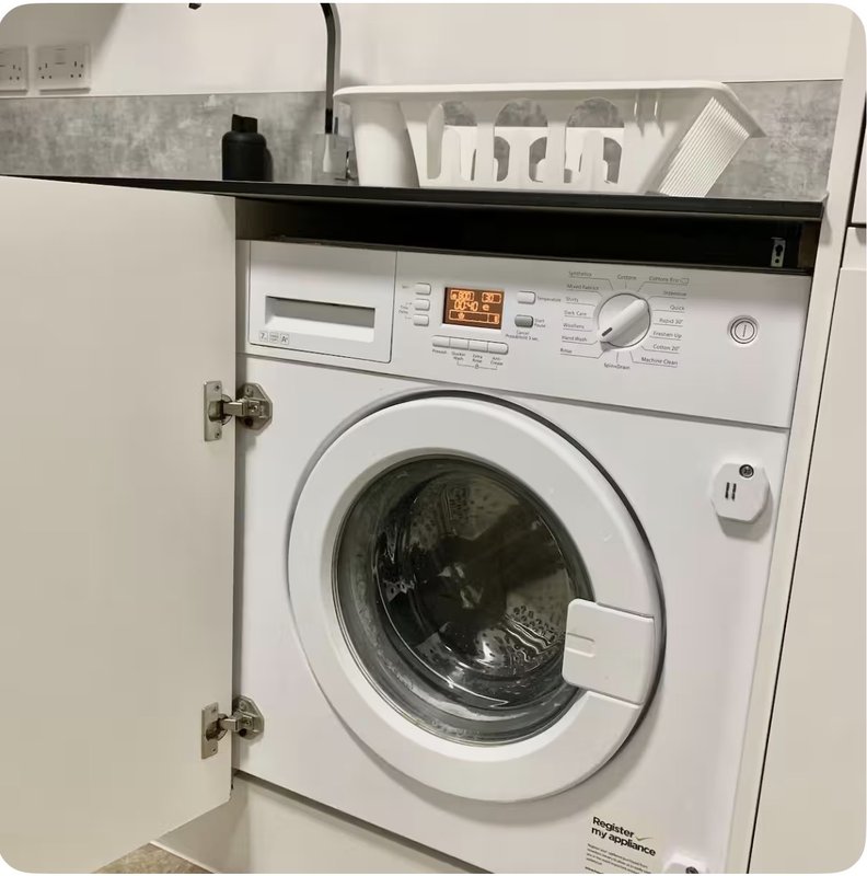 Built-in white washing machine with black countertop and open cupboard doors above