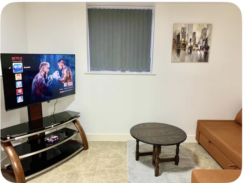 Living room with TV on stand, coffee table, tan sofa, window with blinds, and wall art