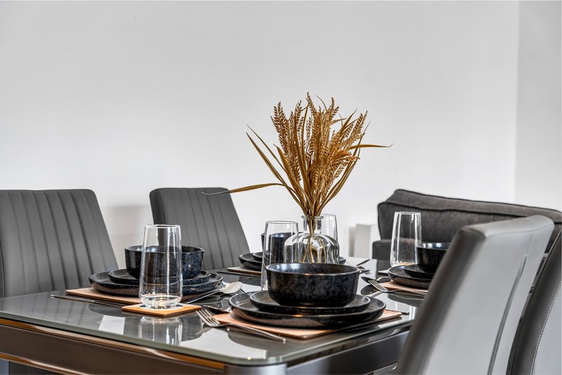 Modern dining table set with gray chairs, place settings, glasses and dried flower centerpiece