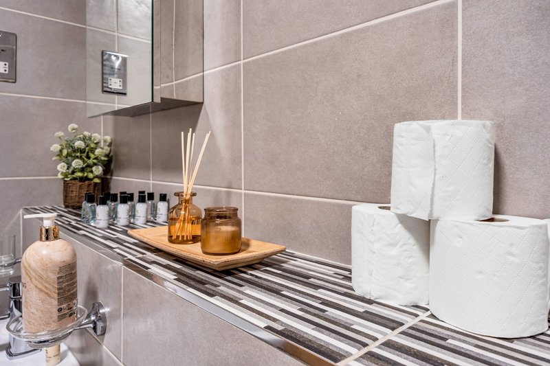Modern bathroom shelf with toiletries, flowers, candles and white towel roll storage
