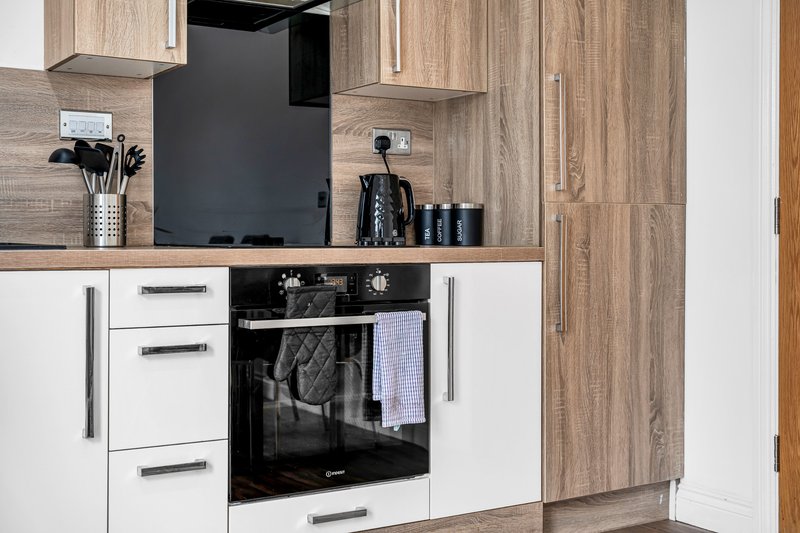 Modern kitchen with white cabinets, wood-grain upper units, black oven and stovetop, stainless steel handles