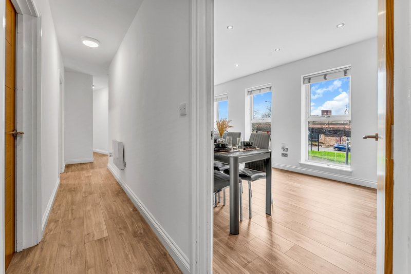 Bright modern hallway with wooden flooring leading to open-plan living area with dining table and large windows