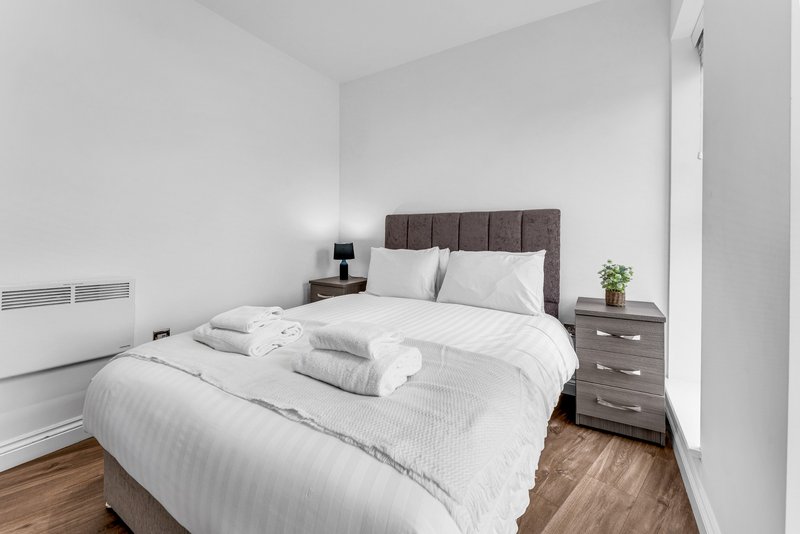 Bright bedroom with double bed, grey upholstered headboard, wooden nightstands, and white bedding