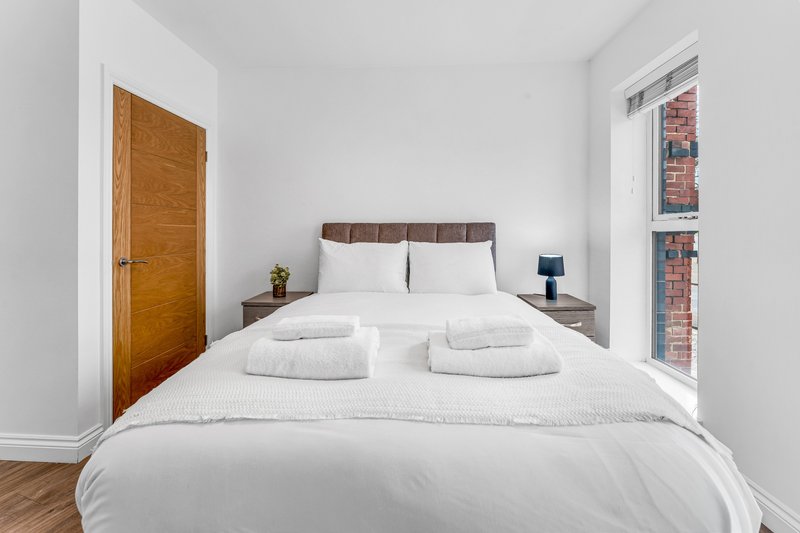 Bright bedroom with double bed, white bedding, wooden door and exposed brick wall