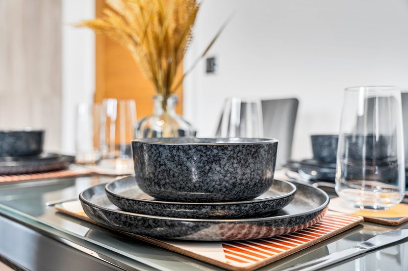 Modern dining table setting with stacked dark plates, glasses, and dried flowers in vase