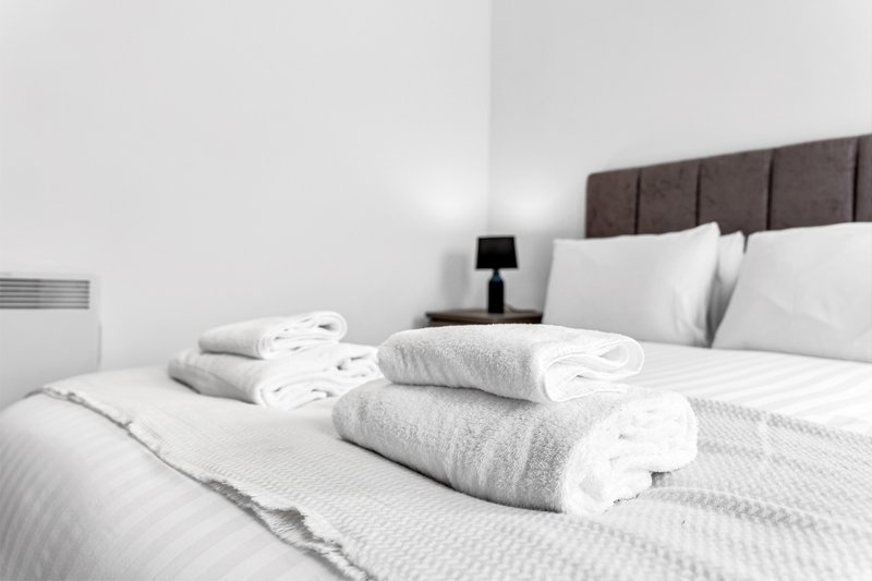 Modern bedroom with neatly rolled towels on bed, upholstered headboard, and side table lamp