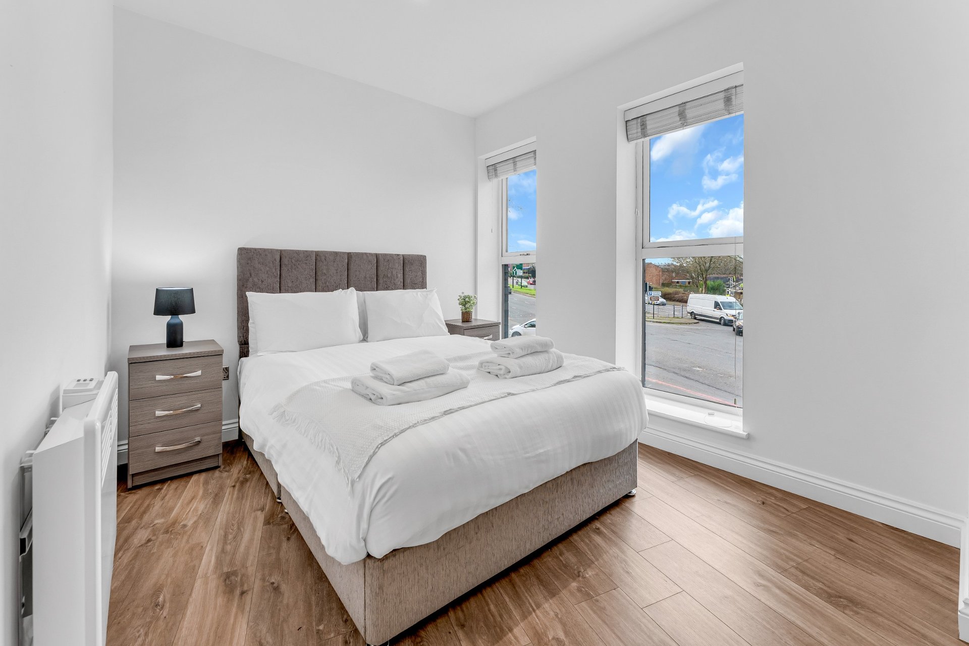 Modern bedroom with double bed, wooden flooring, bedside tables and glass balcony doors