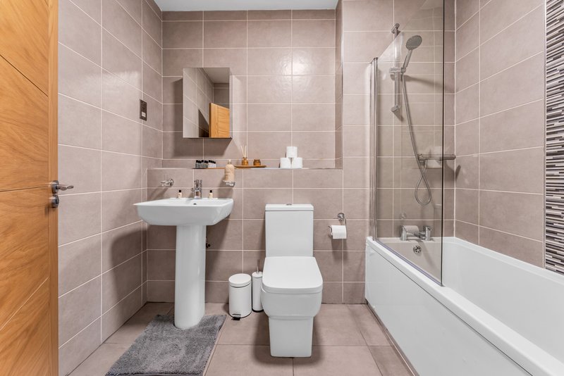 Modern bathroom with pedestal sink, toilet, bathtub with shower screen and heated towel rail