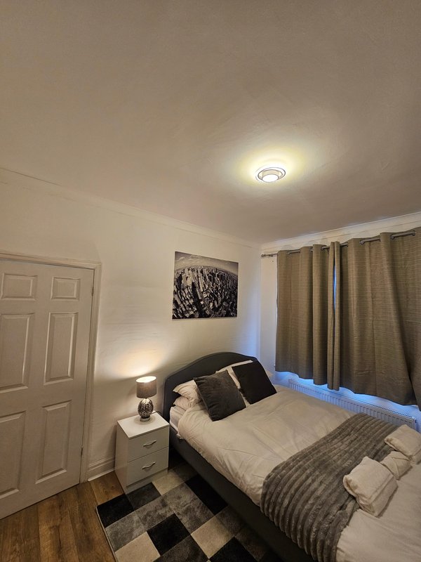 Bedroom with double bed, bedside lamp, white wardrobe, and tan curtains