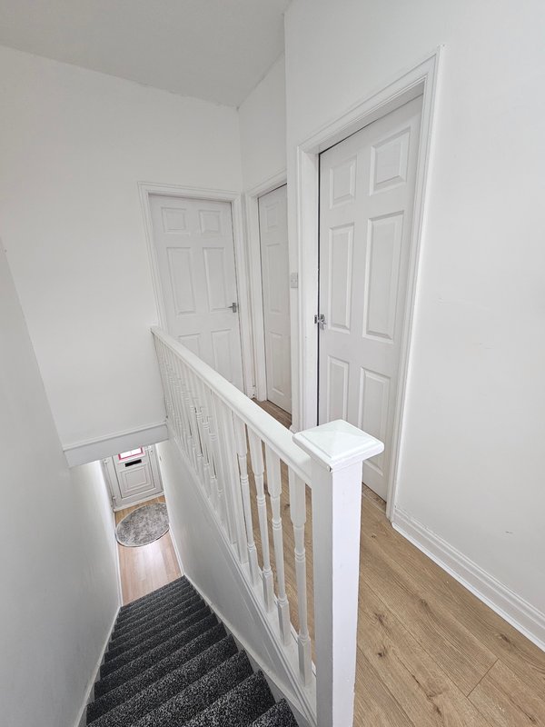 Upstairs hallway with white doors, wooden handrail, and stairs descending on left