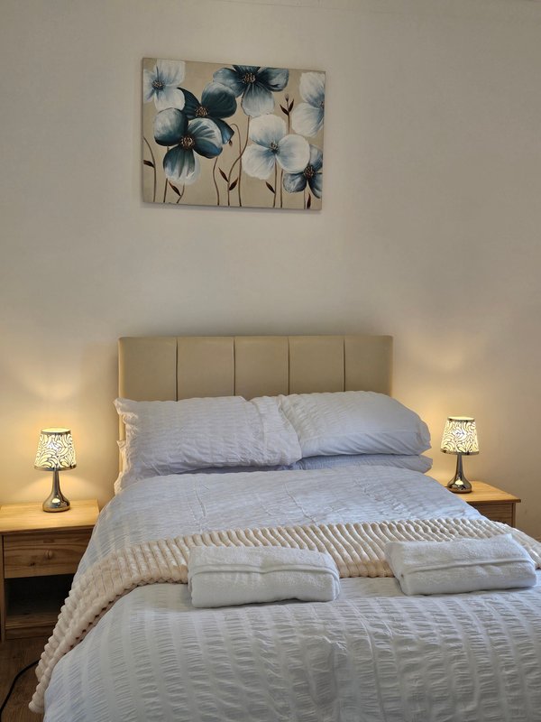 Bedroom with double bed, padded headboard, bedside tables with lamps, and floral wall art