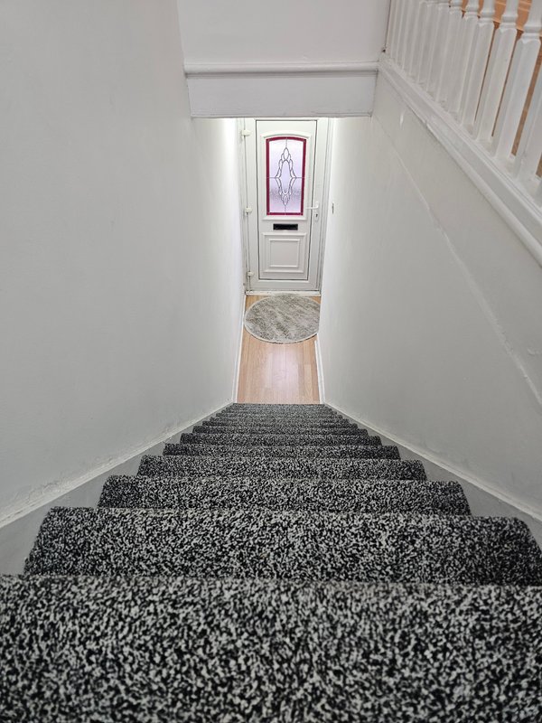 Staircase with dark gray carpet leading to white door with window pane