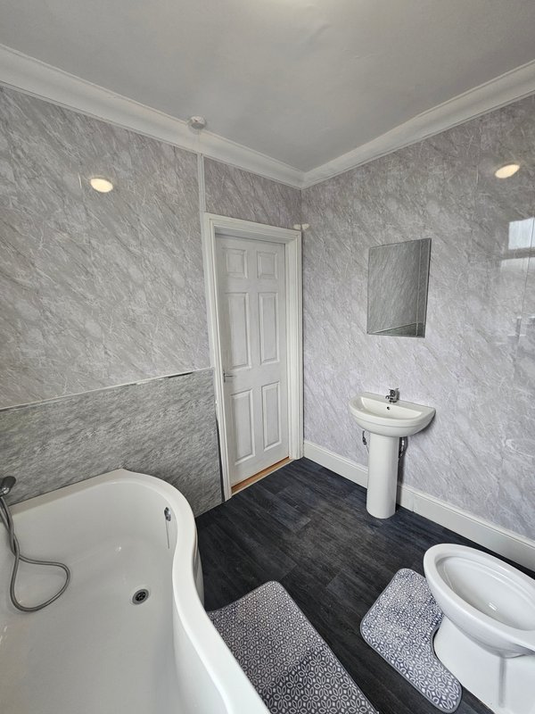 Clean modern bathroom with white bathtub, pedestal sink, toilet, and marble-effect tiling