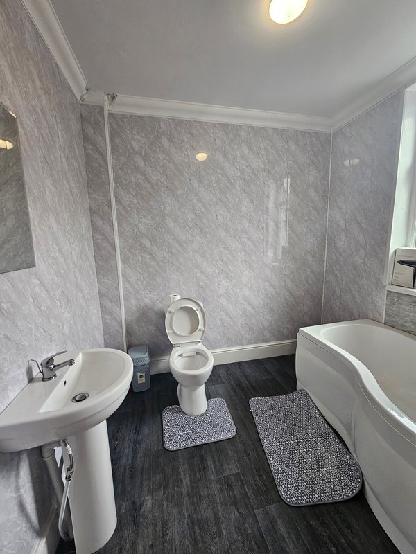 Modern bathroom with pedestal sink, toilet, bathtub, grey tile walls and dark flooring