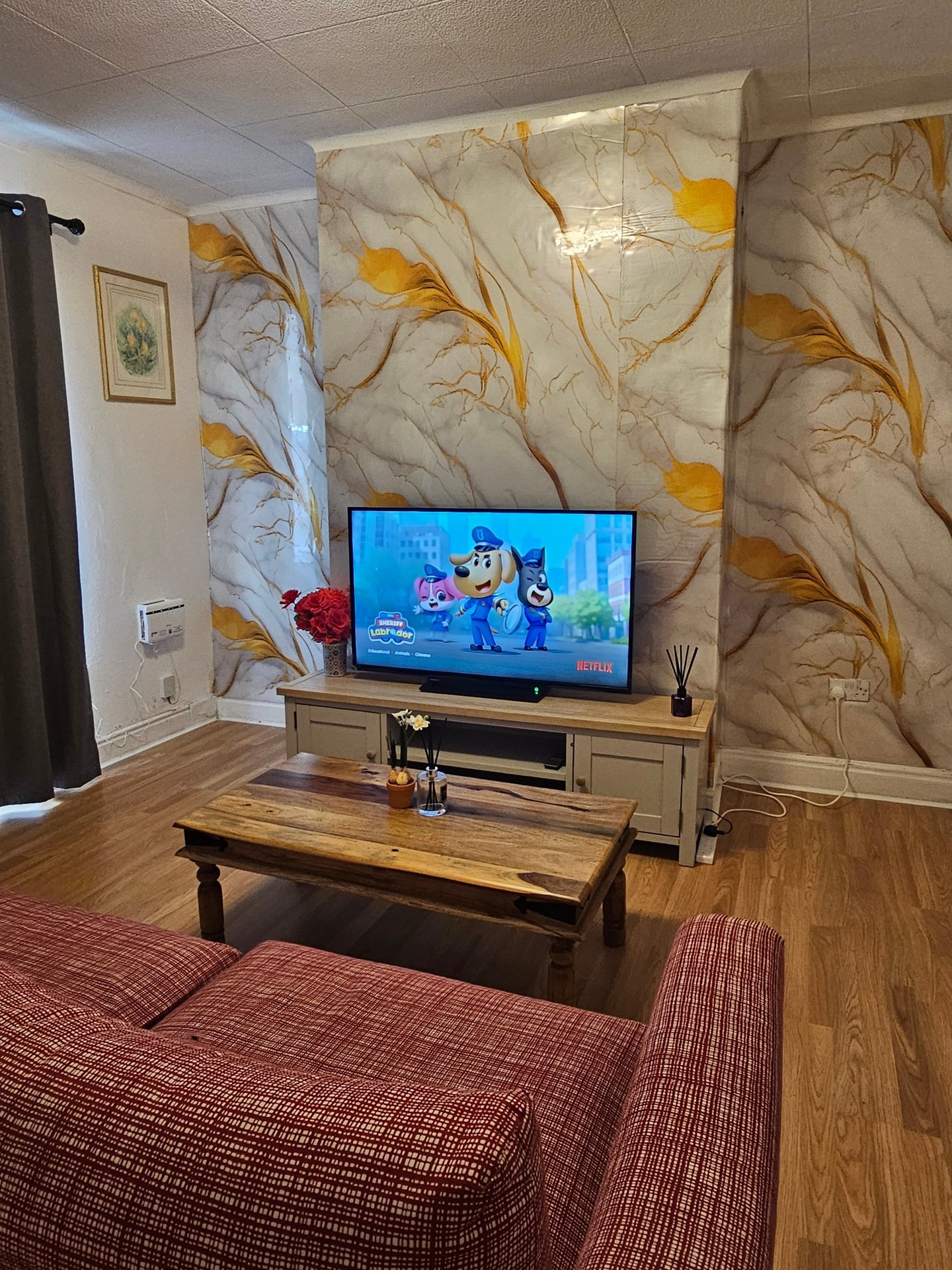 Living room with wall-mounted TV, wooden coffee table, red upholstered seating and decorative wallpaper