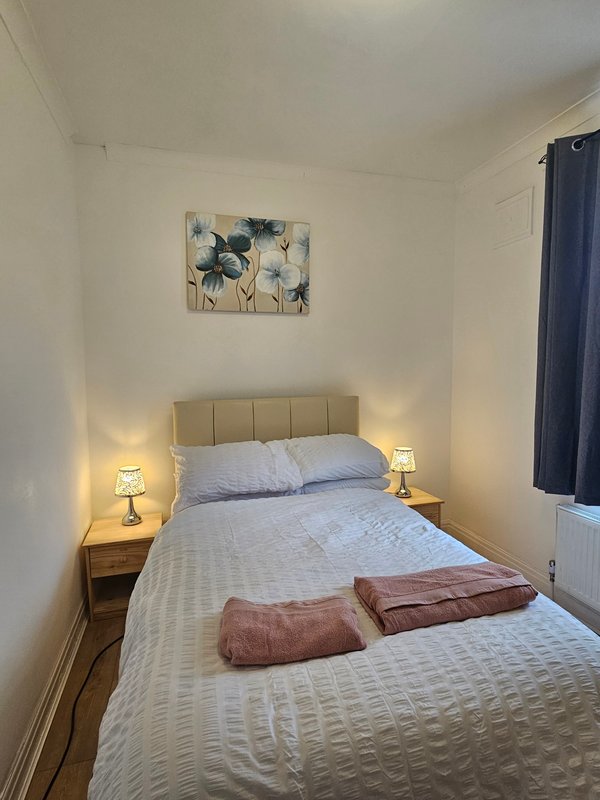 Compact bedroom with double bed, padded headboard, bedside lamps, and framed flower artwork