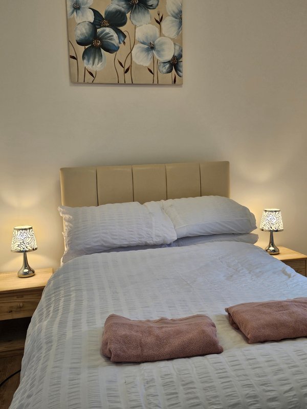 Bedroom with double bed, beige headboard, two bedside lamps and framed flower artwork
