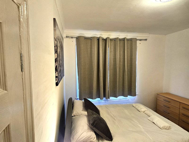 Bedroom with double bed, wooden dresser, curtained window and wall art