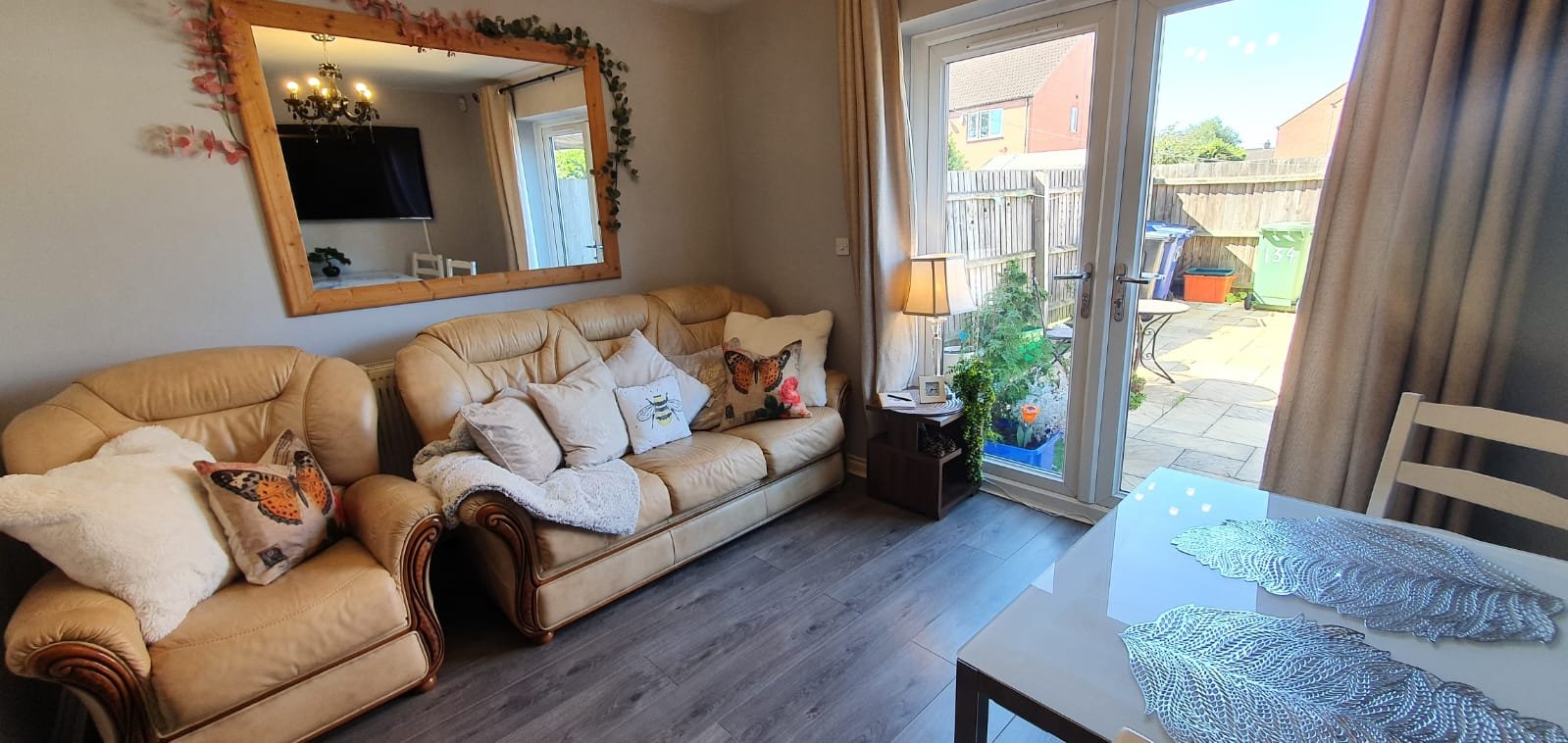 Living room with tan sofa, cushions, mirror, patio doors opening to garden