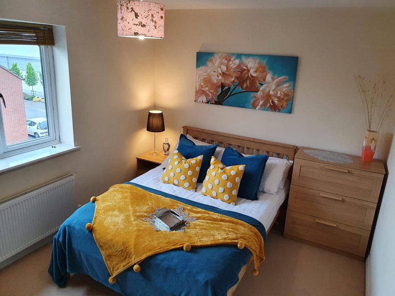 Bedroom with double bed, yellow and blue bedding, wooden furniture, and wall art