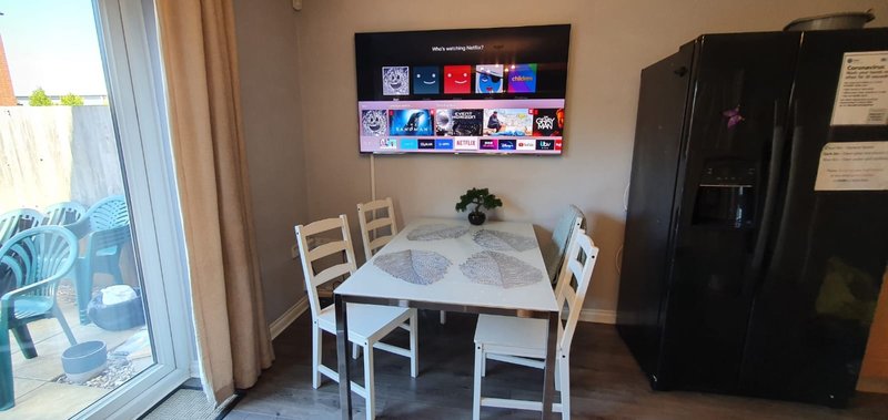 Dining area with white table, chairs, smart TV wall-mounted, and black refrigerator