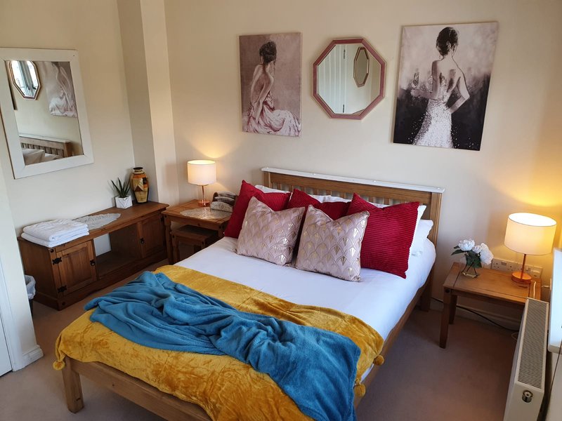 Bedroom with double bed, red pillows, wall art, wooden furniture and bedside lamps