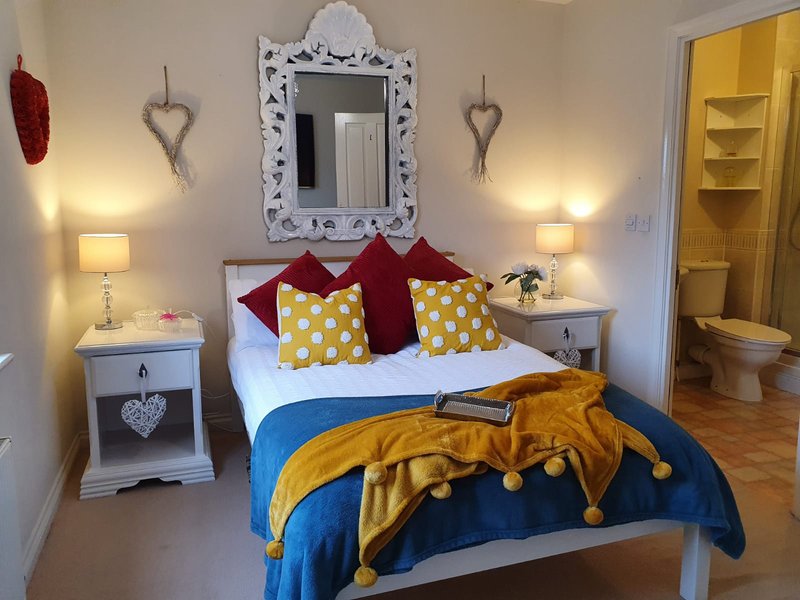 Bedroom with double bed, colorful pillows, bedside tables with lamps, and decorative mirror