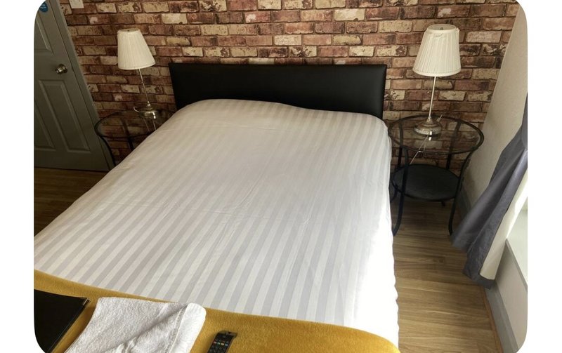 Bedroom with double bed, black headboard, exposed brick wall, bedside lamps and wooden flooring