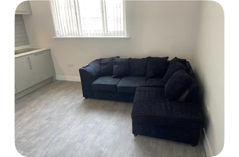 Living room with dark navy corner sofa, laminate flooring, and bright window