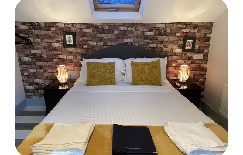 Modern bedroom with double bed, brick feature wall, olive cushions and bedside lamps