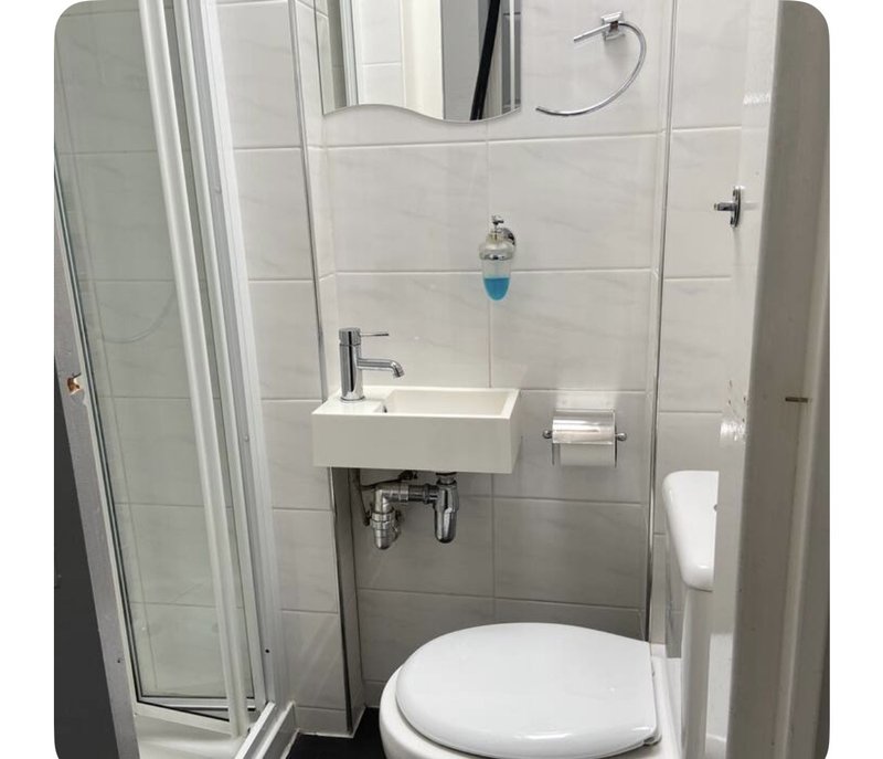 Modern bathroom with white toilet, small sink, mirror and shower enclosure