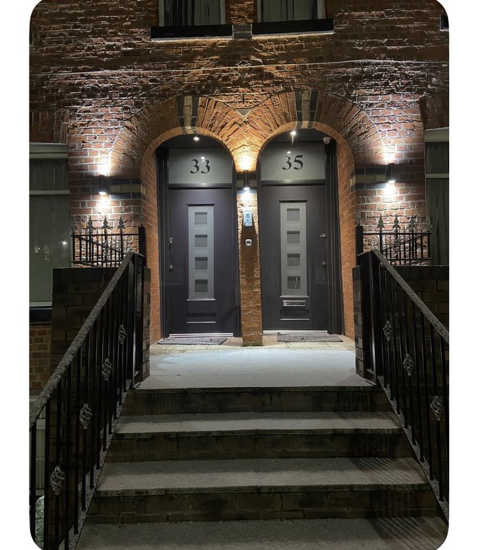 Modern brick building entrance with two dark doors numbered 33 and 35, lit archway, black railings, and steps