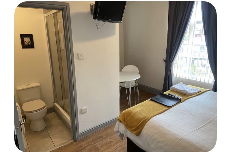 Bedroom with double bed, wall-mounted TV, ensuite bathroom, chair and window with curtains
