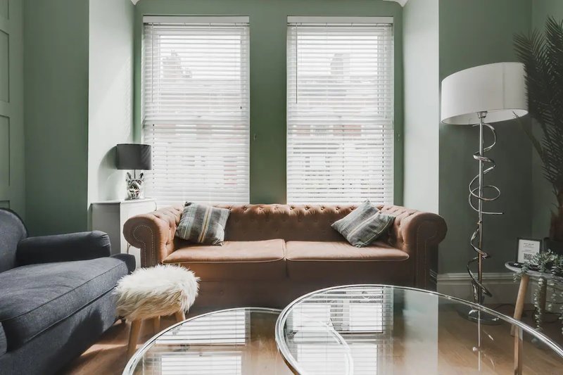 Living room with brown leather sofa, blue armchair, glass coffee table and large windows