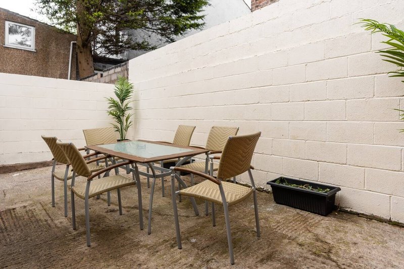Outdoor patio area with metal table, four chairs, potted plant and white brick wall