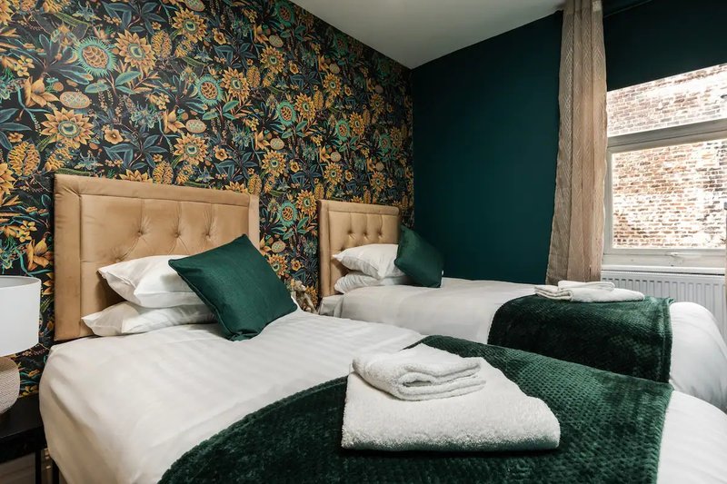 Bedroom with two single beds, patterned wallpaper, upholstered headboards, and green accents