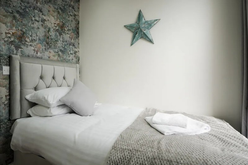 Bedroom with single bed, grey headboard, white pillows, textured throw, and decorative star