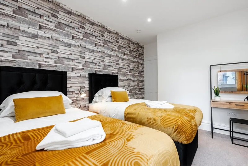 Modern bedroom with twin beds, yellow bedding, brick feature wall and desk area