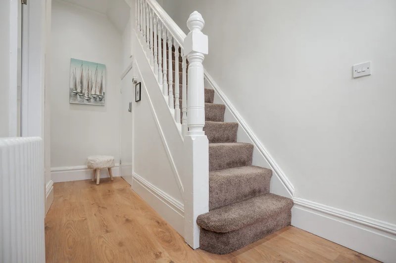 Hallway with wooden flooring, white staircase with grey carpet treads and small framed artwork on wall