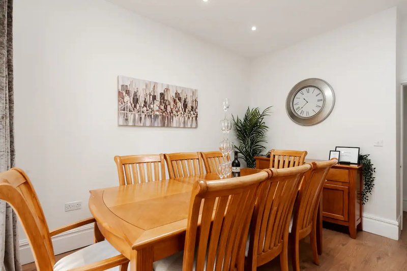 Dining room with wooden table, six chairs, wall art, clock and potted plant