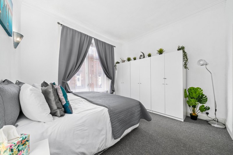 Bright bedroom with double bed, grey curtains, white wardrobes and potted plants