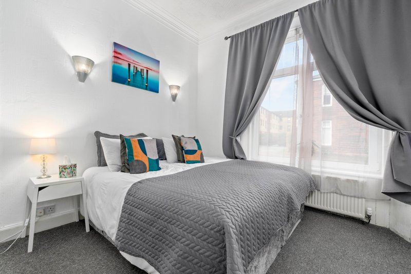 Modern bedroom with double bed, colorful cushions, bedside table, wall art and grey curtains