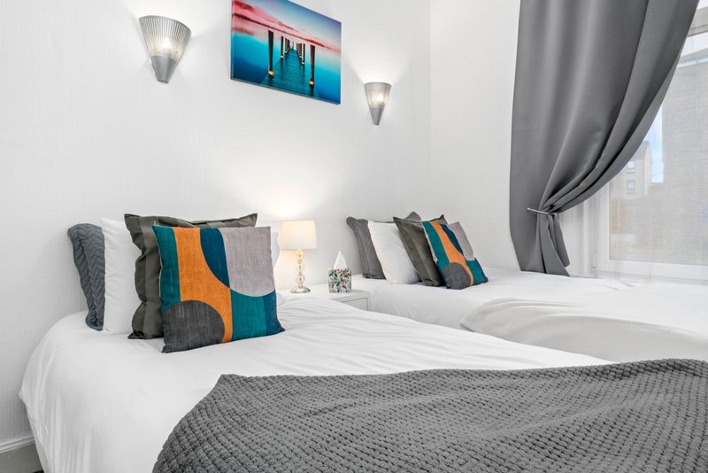 Modern bedroom with twin beds, colorful pillows, wall art, and grey curtains