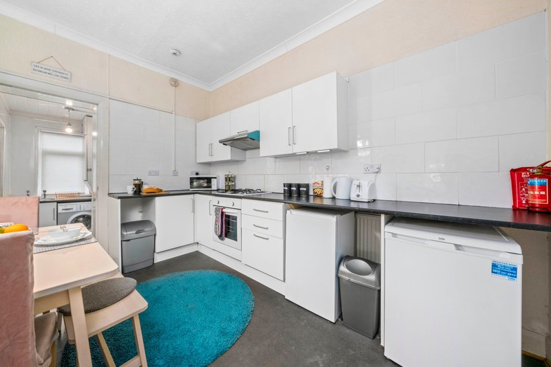 Modern kitchen with white cabinetry, black worktops, integrated appliances and turquoise rug