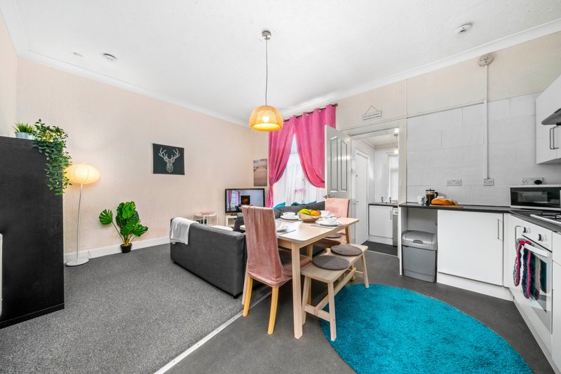 Open-plan living area with kitchen, dining table, sofa and colorful soft furnishings