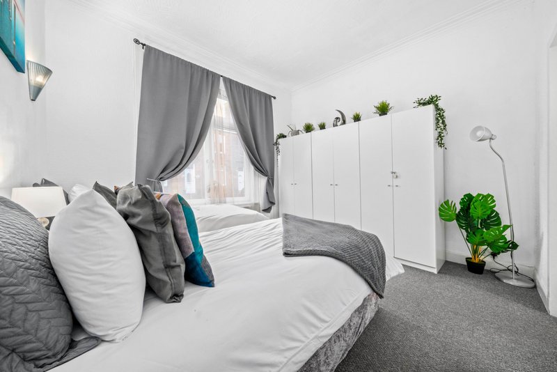 Bright modern bedroom with two single beds, grey bedding, white wardrobe and potted plants