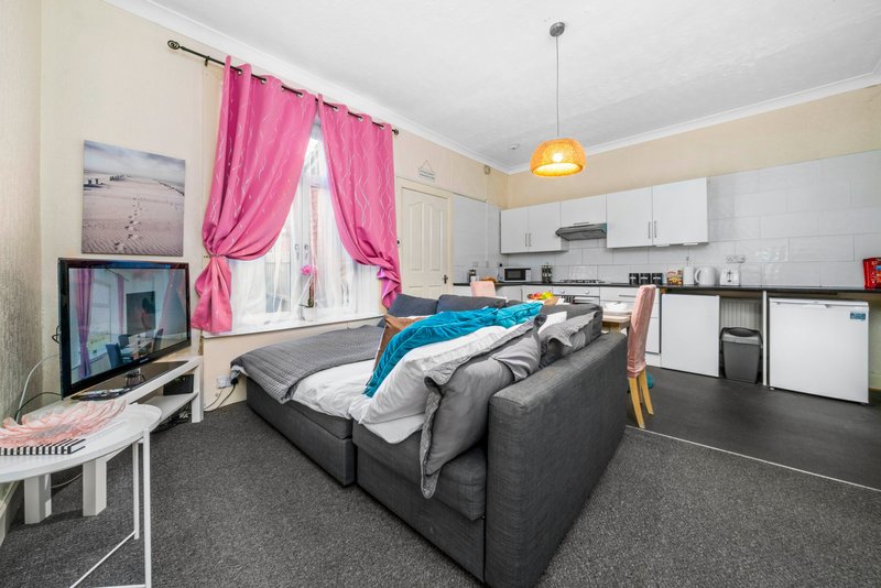 Studio apartment with grey sofa, kitchen area, pink curtains and bedroom space