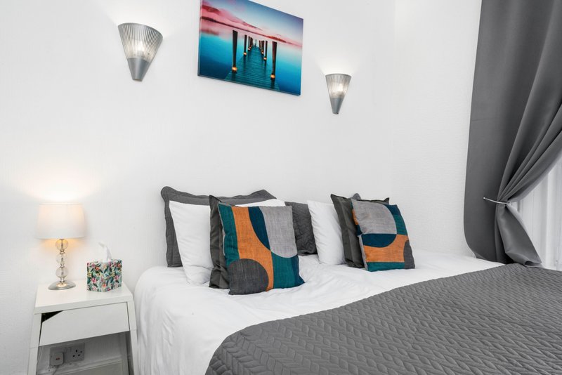 Modern bedroom with double bed, colorful pillows, wall art, bedside lamp and sconces